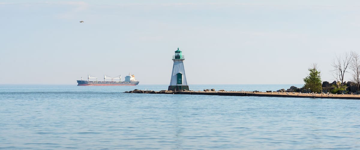 A lighthouse on a pier with a cargo ship in the background.