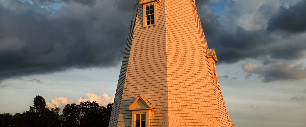 A tall lighthouse with a green top, set against a dramatic sky with clouds.