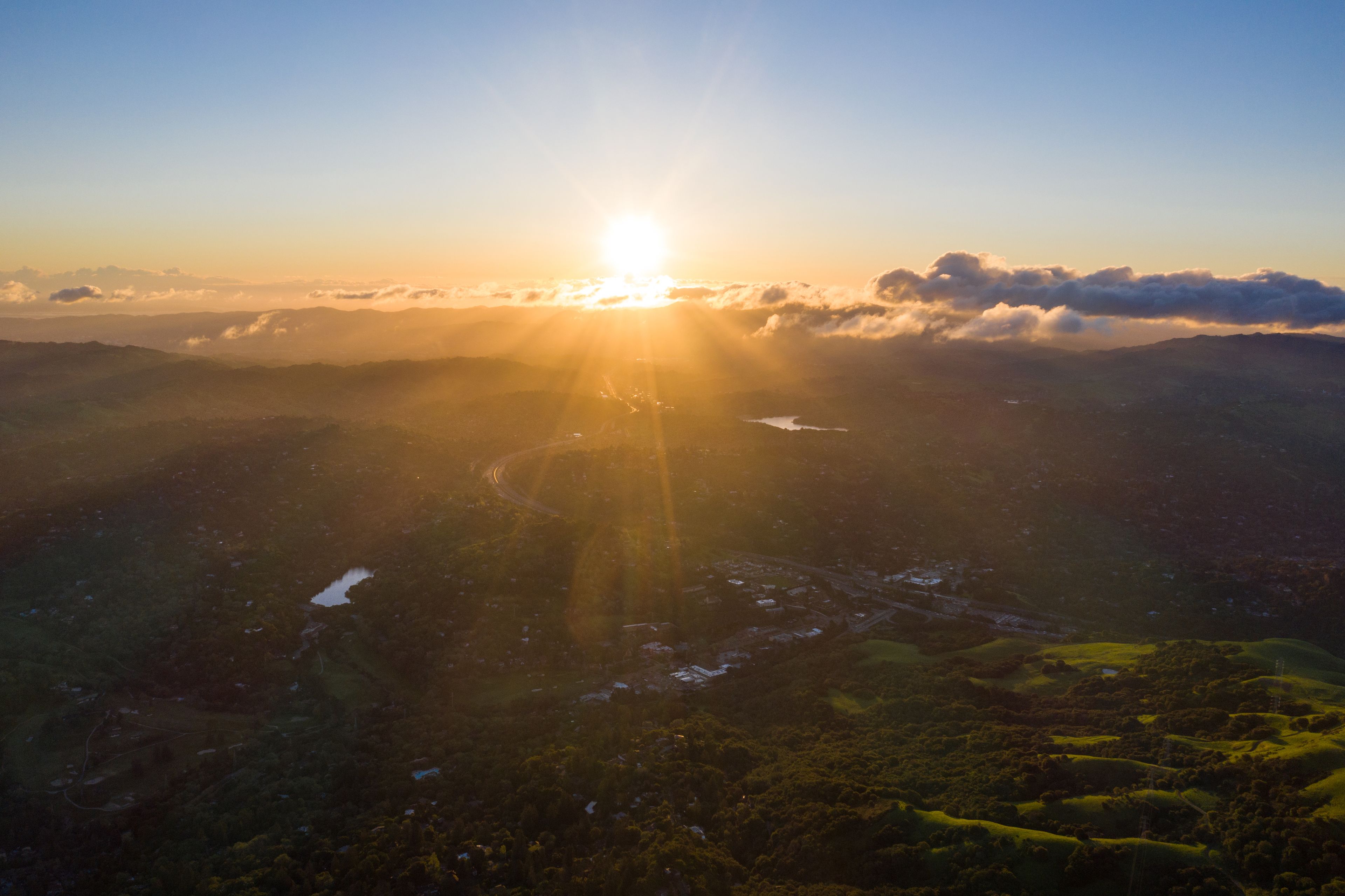 A sunrise over a mountainous landscape with a winding road and a lake.