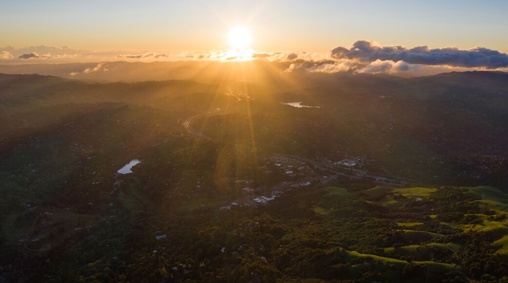 A sunrise over a mountainous landscape with a winding road and a lake.