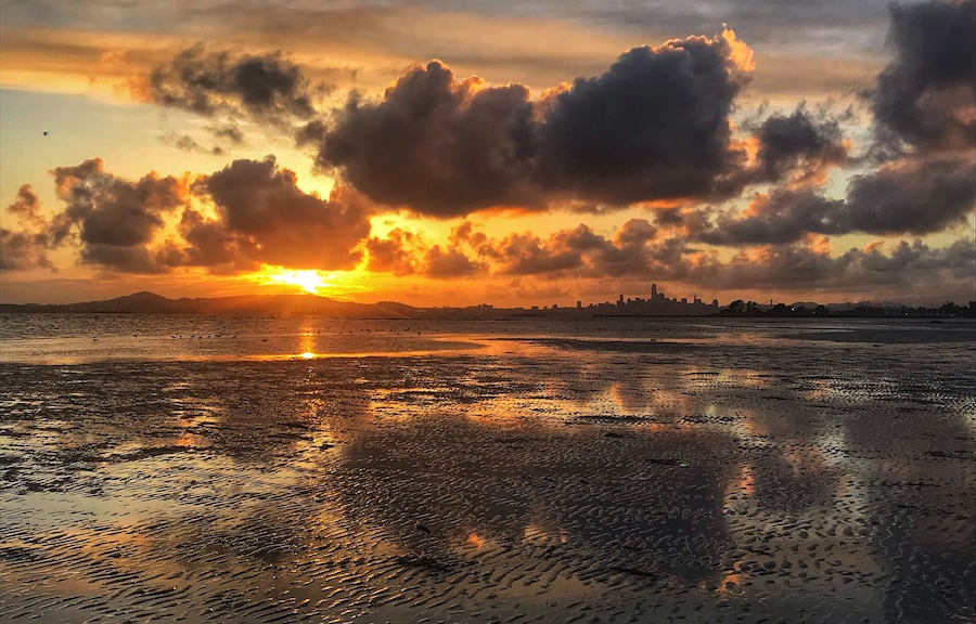 A sunset over a wet beach with a city skyline in the distance.