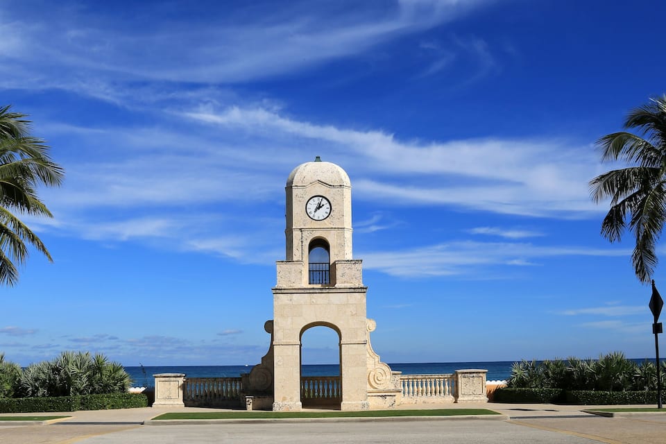 A clock tower with a clock face, surrounded by palm trees and a clear blue sky.