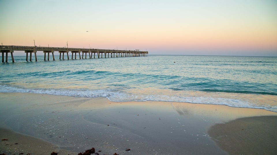 A beach with waves, a pier extending into the water, and a sunset sky.