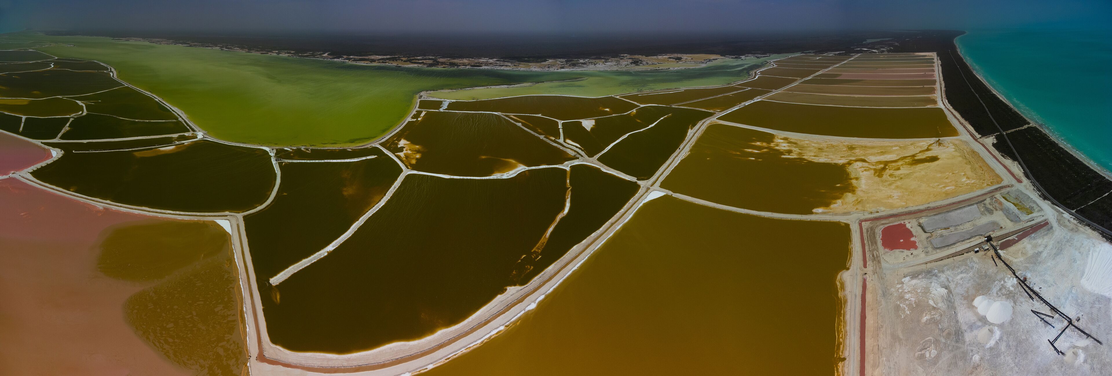 A salt flat with distinct color variations and bordered by a coastline.