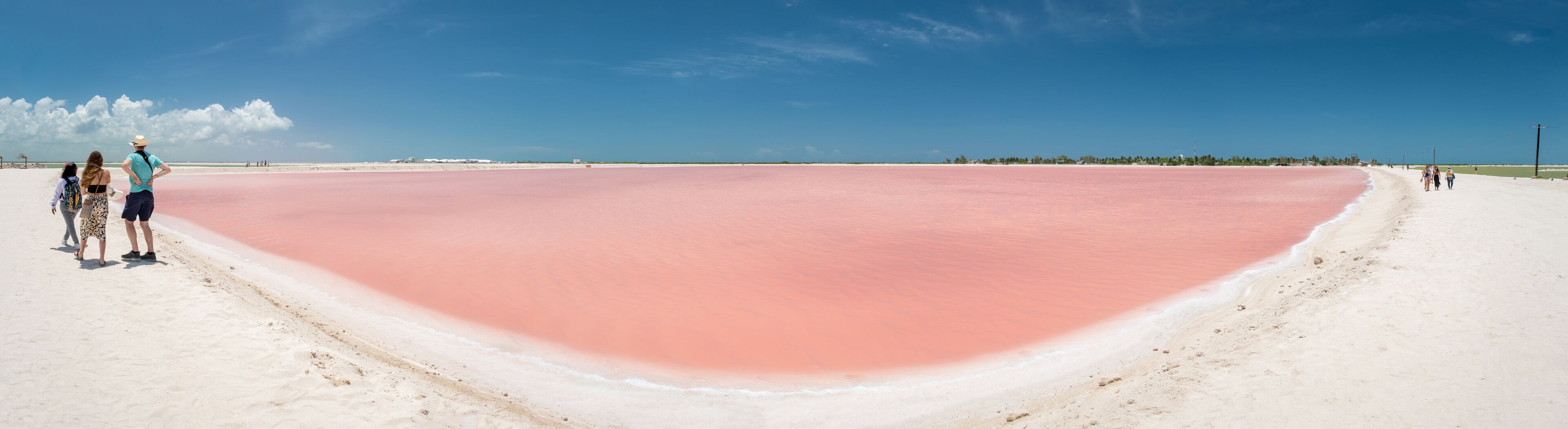 Pink lake with white salt near the shore. In the background, a salt factory against a blue sky. Las Coloradas, Yucatan, Mexico
