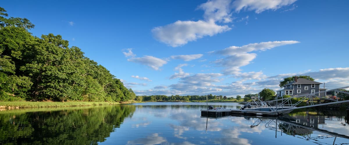 A calm lake with a dock, a house on the right, and dense trees on the left.