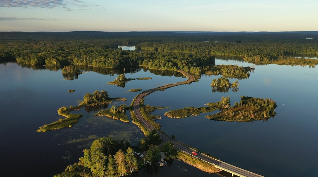 Establishing shot of american wilderness. Aerial view of scenic road through lake, and wooded islands. Calm morning water, dawn sky, view from above.