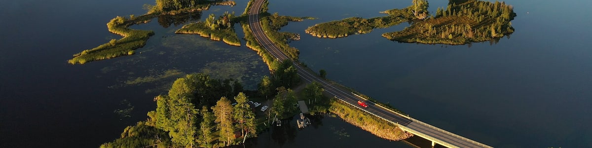 Establishing shot of american wilderness. Aerial view of scenic road through lake, and wooded islands. Calm morning water, dawn sky, view from above.