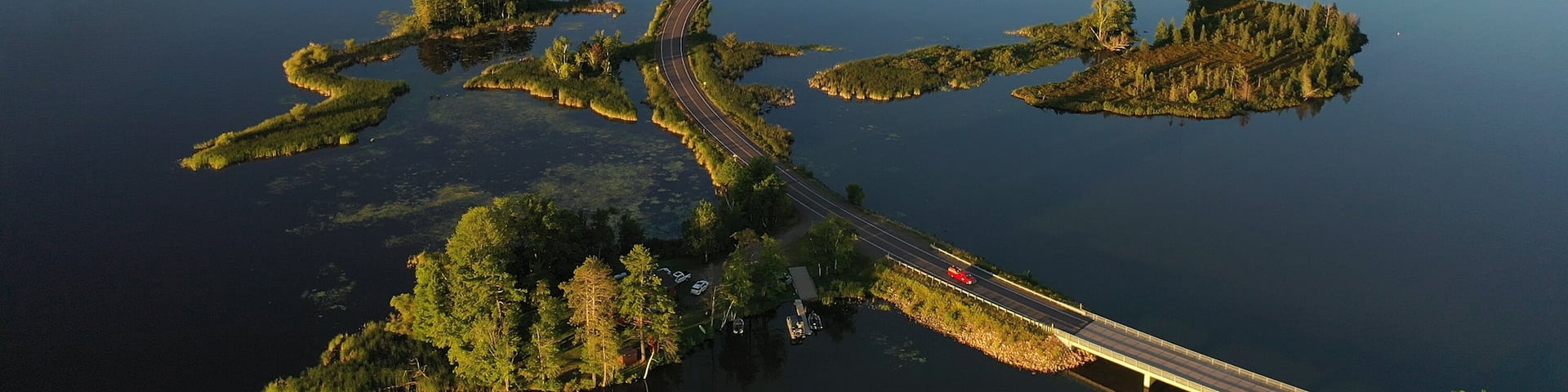 Establishing shot of american wilderness. Aerial view of scenic road through lake, and wooded islands. Calm morning water, dawn sky, view from above.