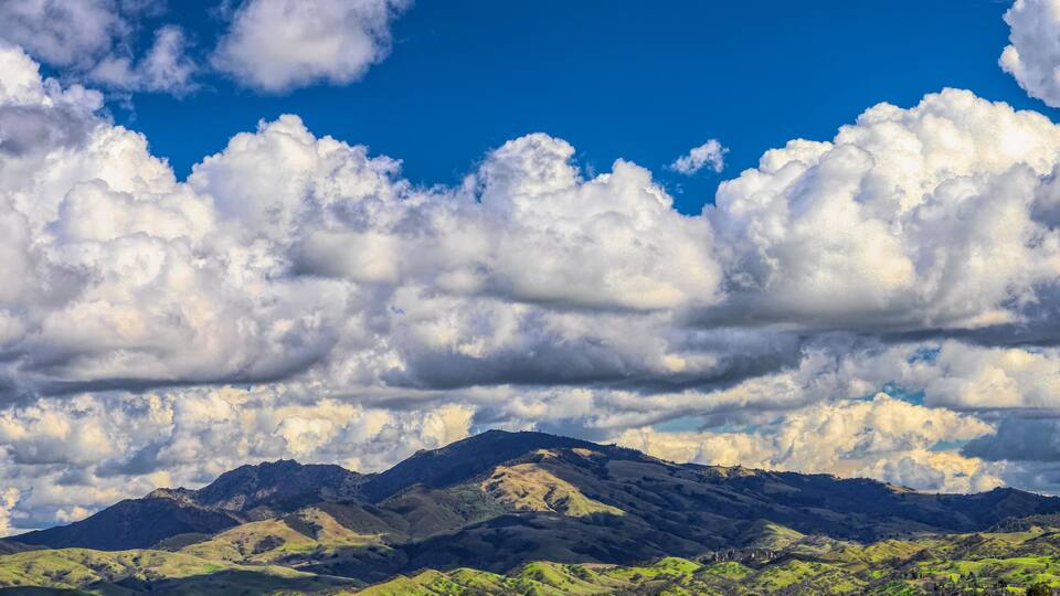 A mountainous landscape with rolling hills and a clear blue sky with fluffy clouds.