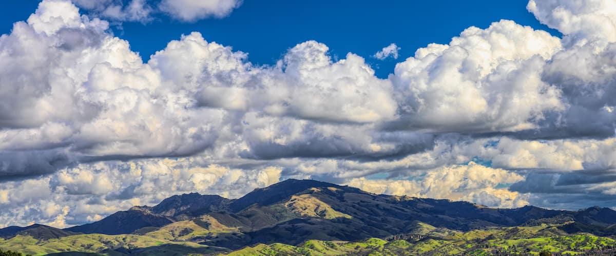 A mountainous landscape with rolling hills and a clear blue sky with fluffy clouds.
