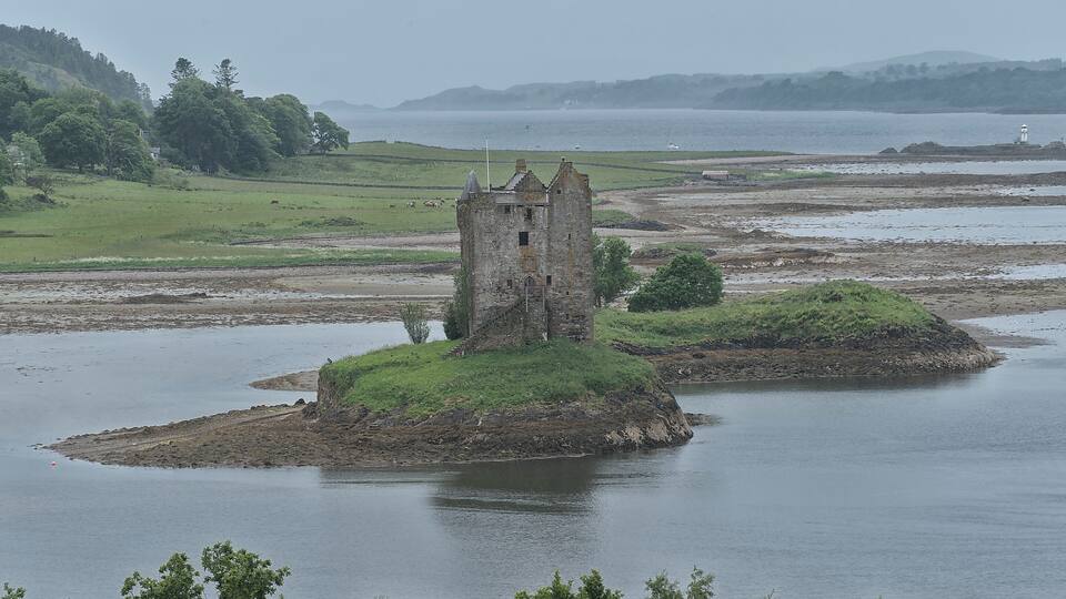 A historic tower on a small island surrounded by water, with a lighthouse in the distance.