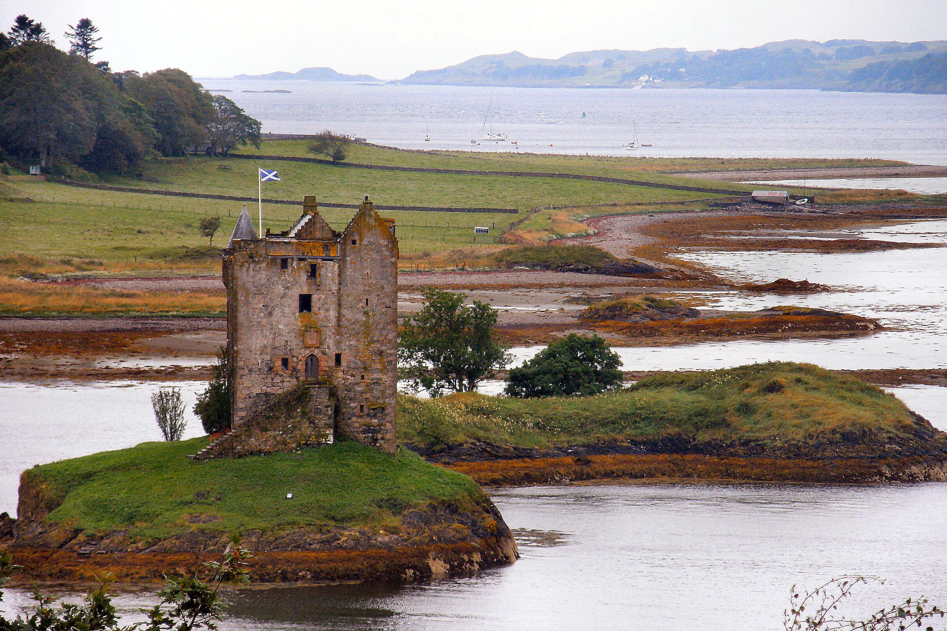 A historic stone tower on a grassy island surrounded by water.