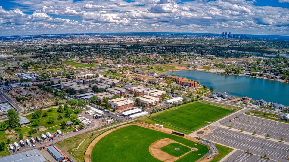 An aerial view of a city with a large green park, a baseball field, and a body of water.