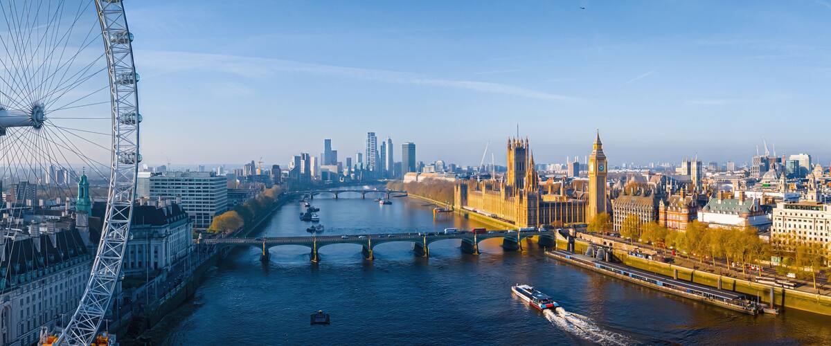 A large Ferris wheel, a river with bridges, and historic buildings including a prominent clock tower.