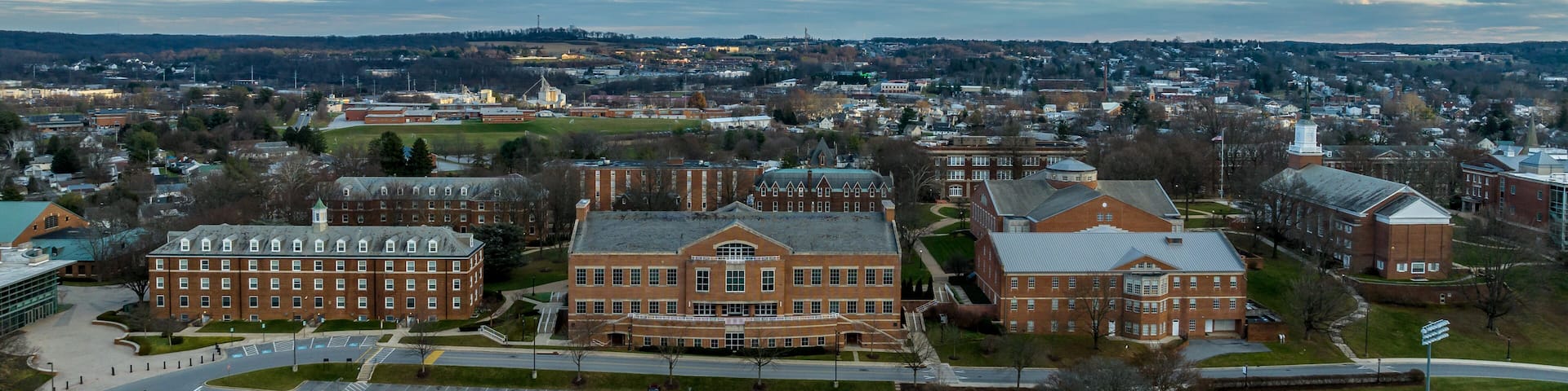 A large campus with multiple brick buildings, a parking lot, and a surrounding urban area.