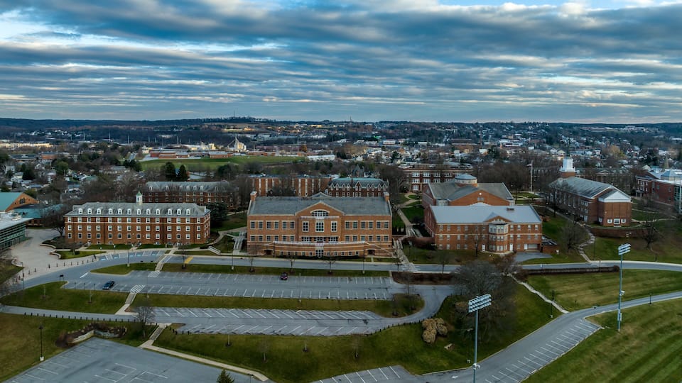 A large campus with multiple brick buildings, a parking lot, and a surrounding urban area.