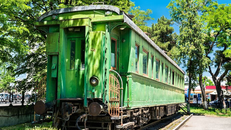 A green train car parked on tracks with trees and buildings in the background.