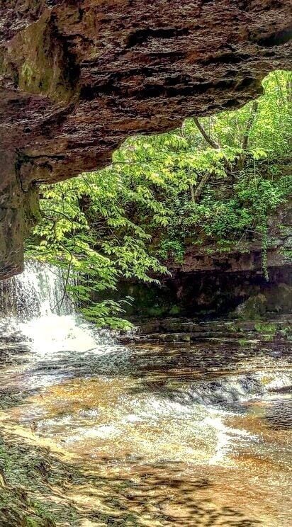 A waterfall cascading through a rocky gorge with lush green foliage above.