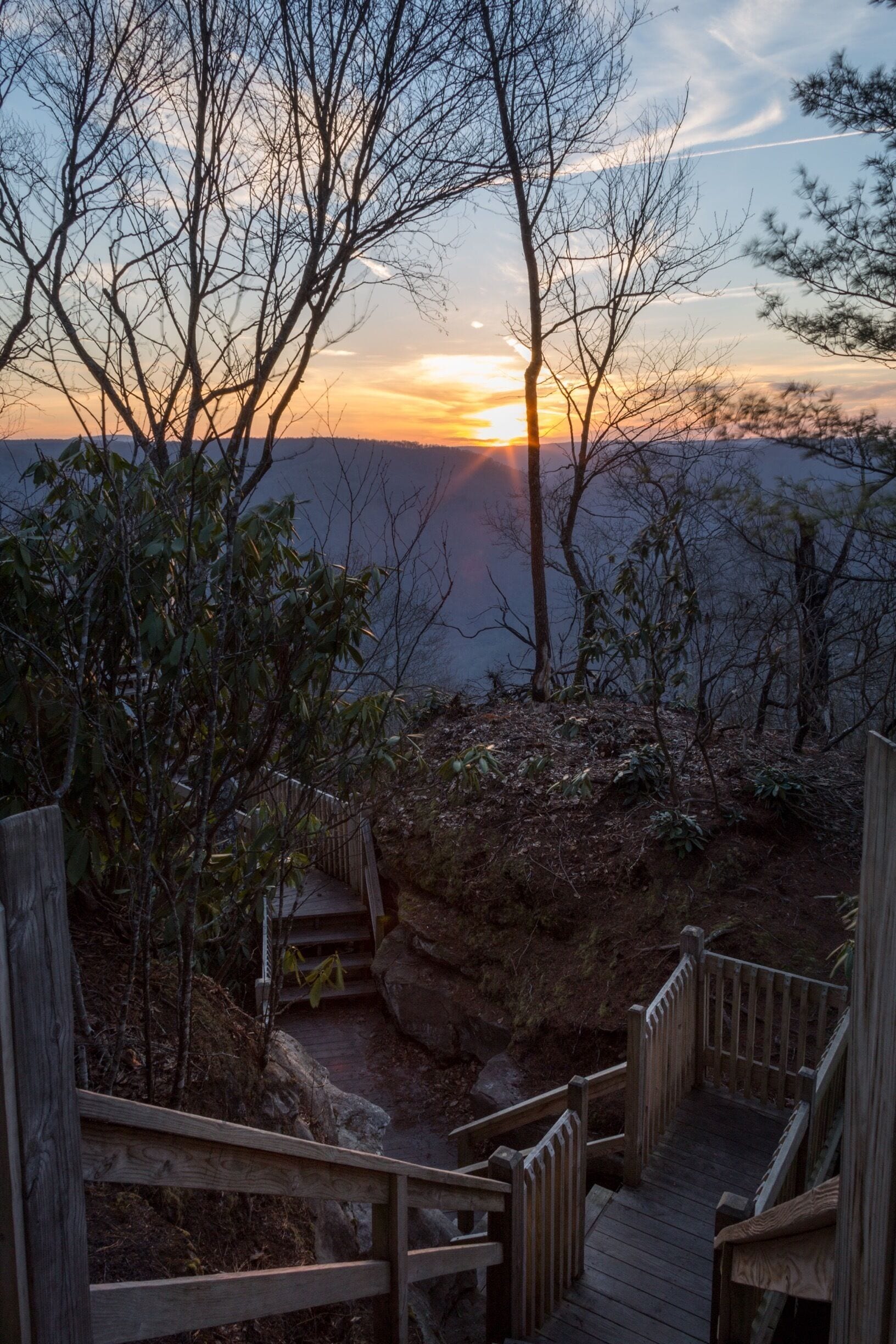 A wooden staircase leading to a scenic overlook with a sunset in the background.