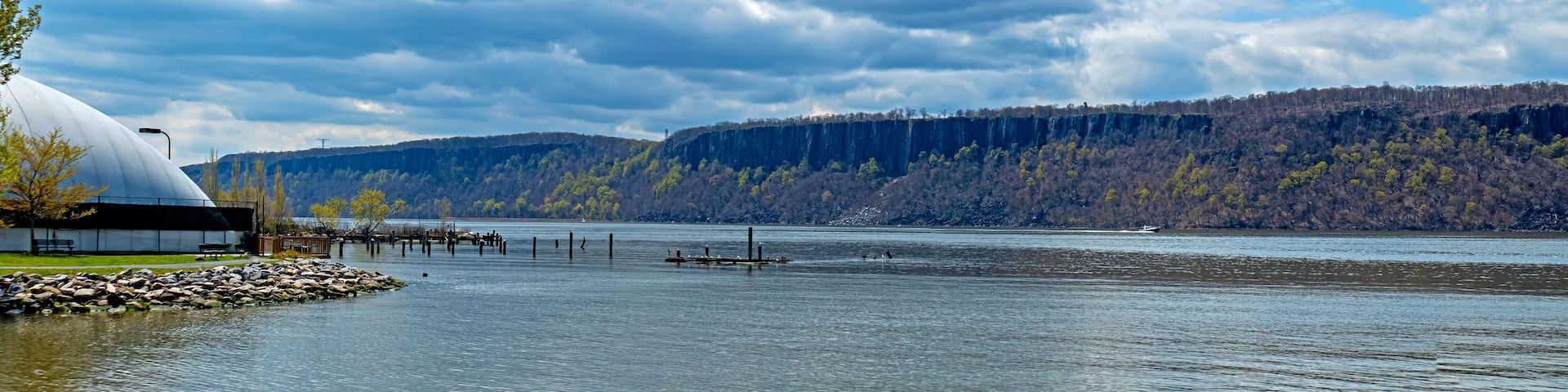 A lake with a dome-shaped building, wooden docks, and a forested hillside in the background.