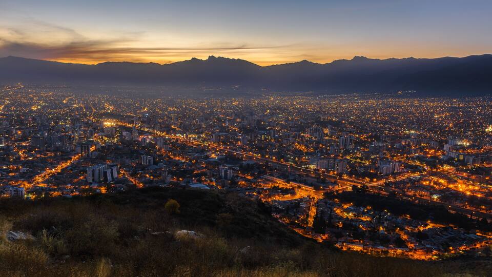 A cityscape at dusk with illuminated streets and distant mountains.