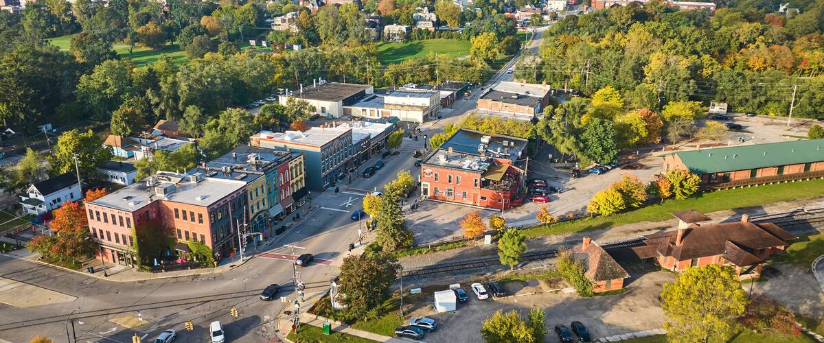 An aerial view of a town with historic buildings, a railroad track, and surrounding greenery.