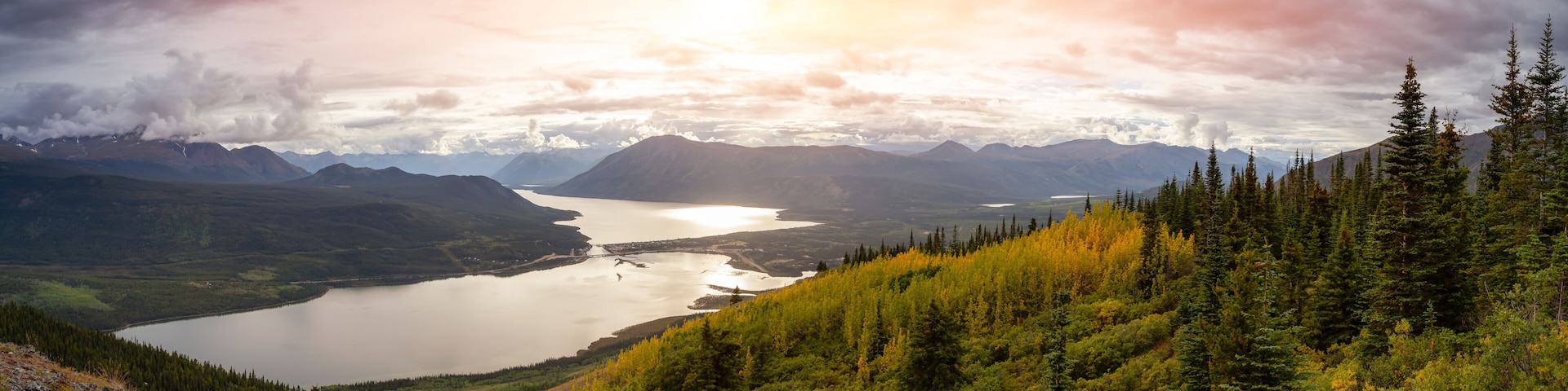 A mountainous landscape with a lake, dense forest, and a sunset.