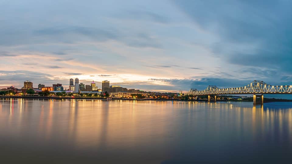 A city skyline with a prominent bridge spanning a calm river, reflecting the city lights.