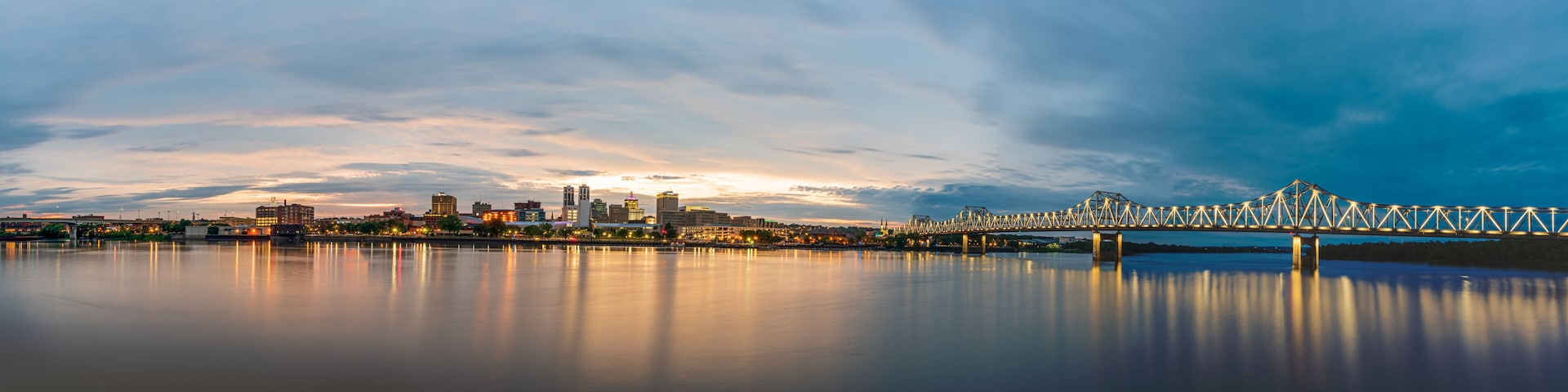 A city skyline with a prominent bridge spanning a calm river, reflecting the city lights.