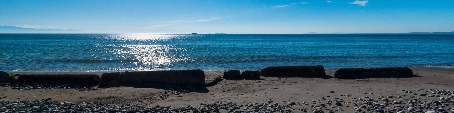 A beach with pebbles and a calm sea under a clear blue sky.