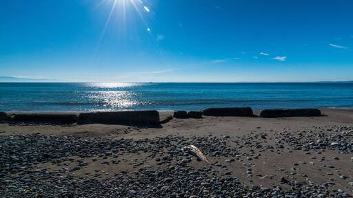 A beach with pebbles and a calm sea under a clear blue sky.
