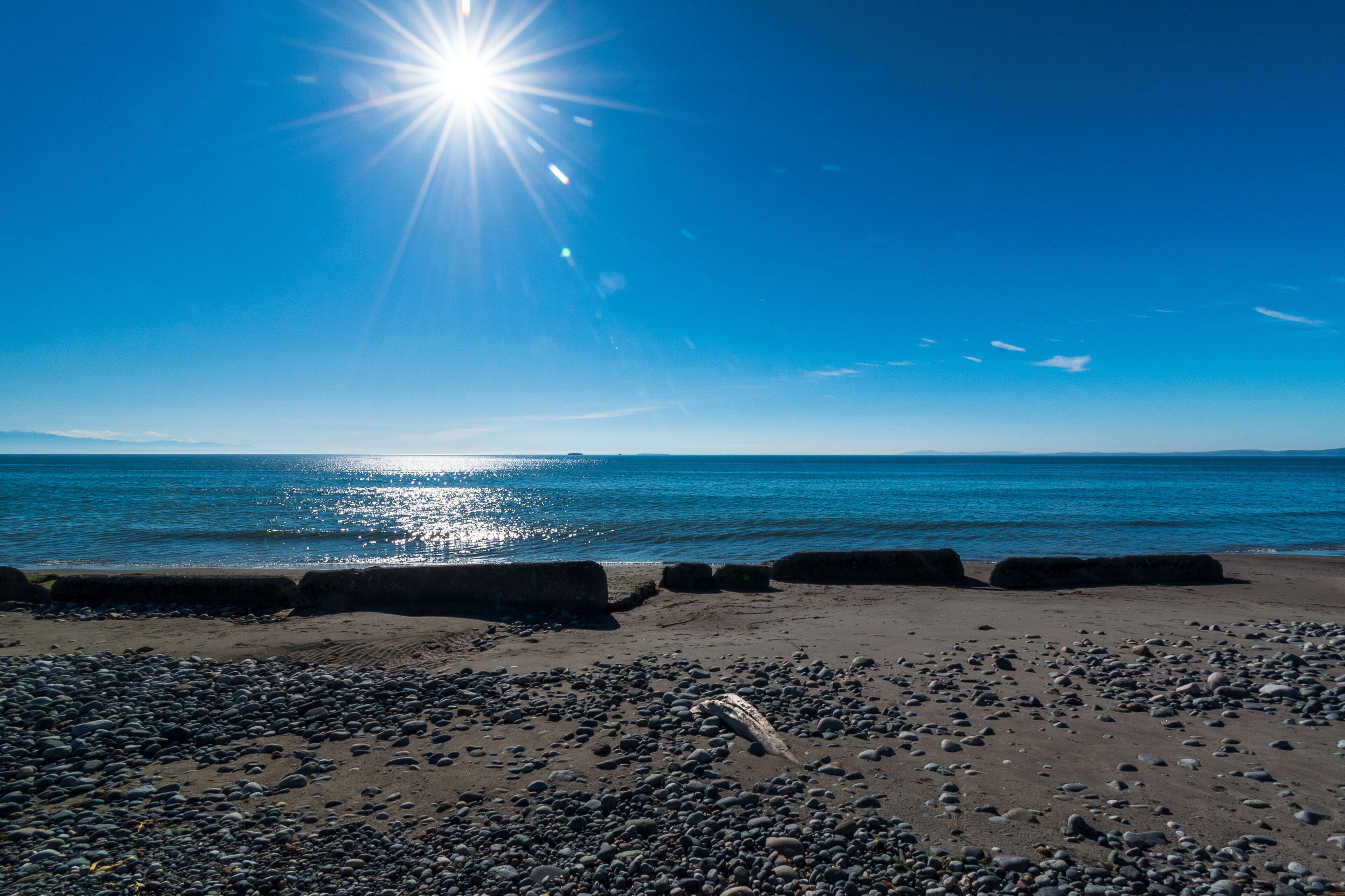 A beach with pebbles, calm water, and a clear sky.
