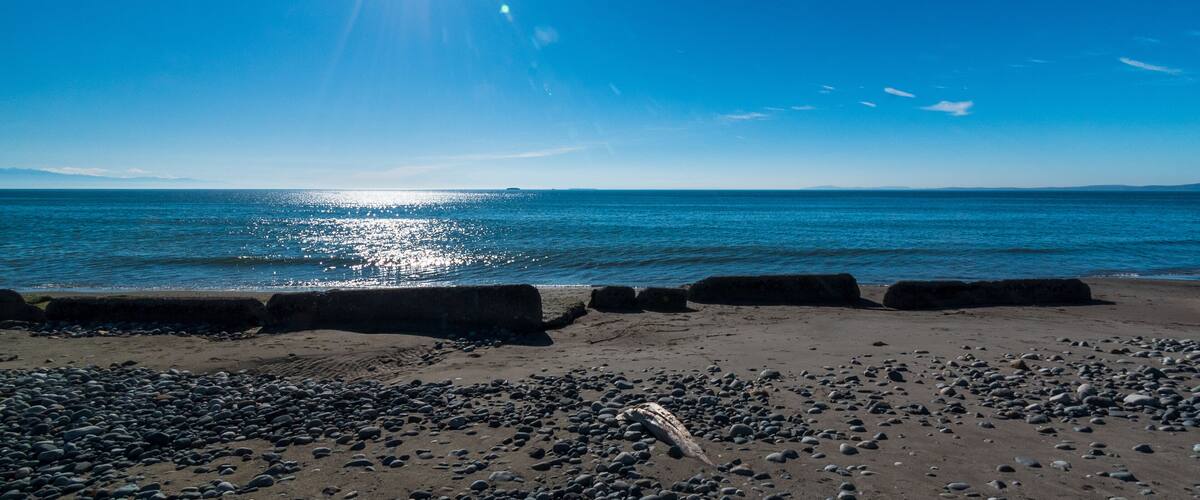 A beach with pebbles, calm water, and a clear sky.