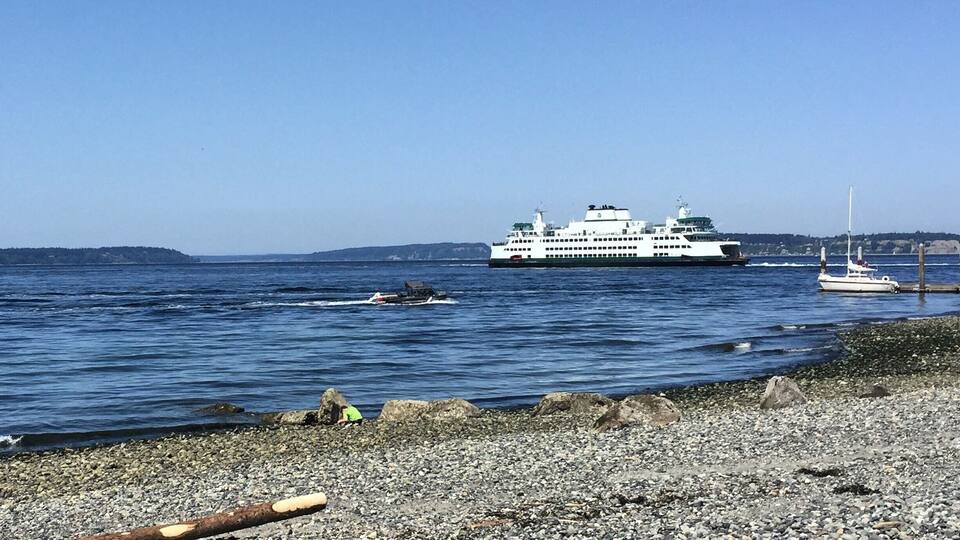 Un ferry en un mar tranquilo, una costa rocosa y una masa de tierra distante.