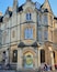 Un bâtiment historique en pierre, doté de fenêtres en arc de cercle et d’un emblème circulaire bien visible à l’entrée.
