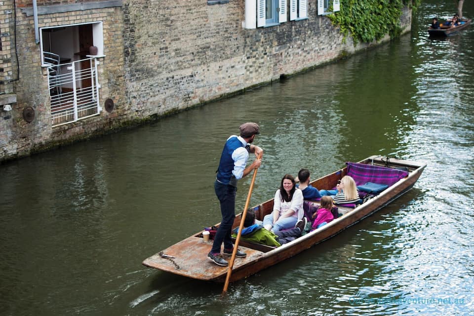 A narrow canal with a wooden boat being rowed by a man.