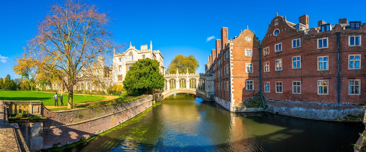 Un canal con un puente, un edificio histórico y un camino bordeado de árboles.