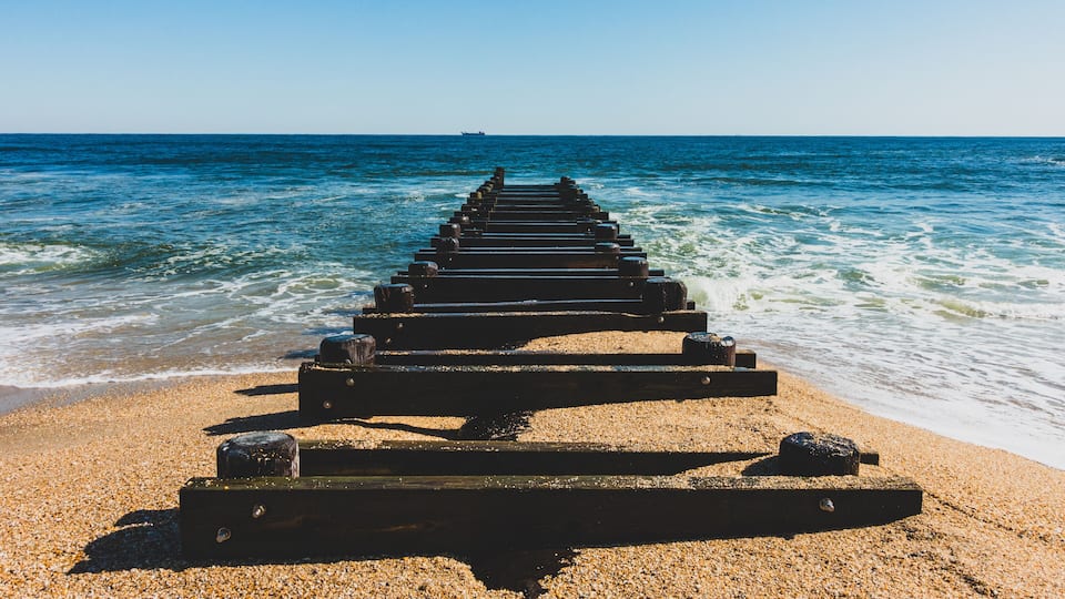 A wooden pier extending into the sea with pebbles on the beach.