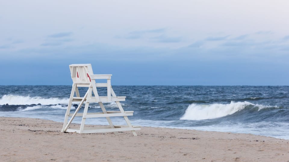 A beach with a lifeguard chair and waves in the background.