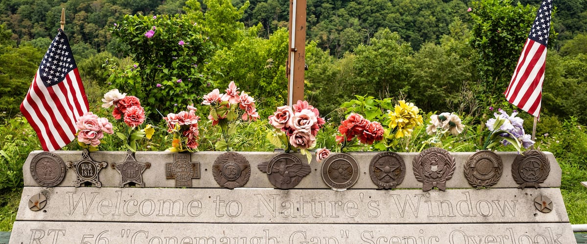 A memorial sign with American flags and flowers, surrounded by lush greenery.