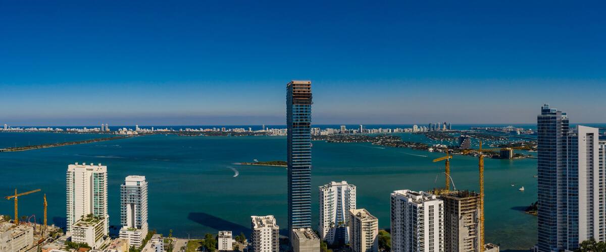 A coastal cityscape with high-rise buildings, a bridge, and a clear blue sky.