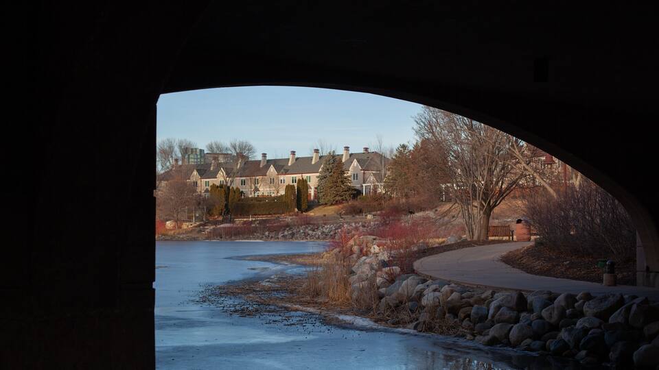 A frozen river under a bridge with houses in the background.