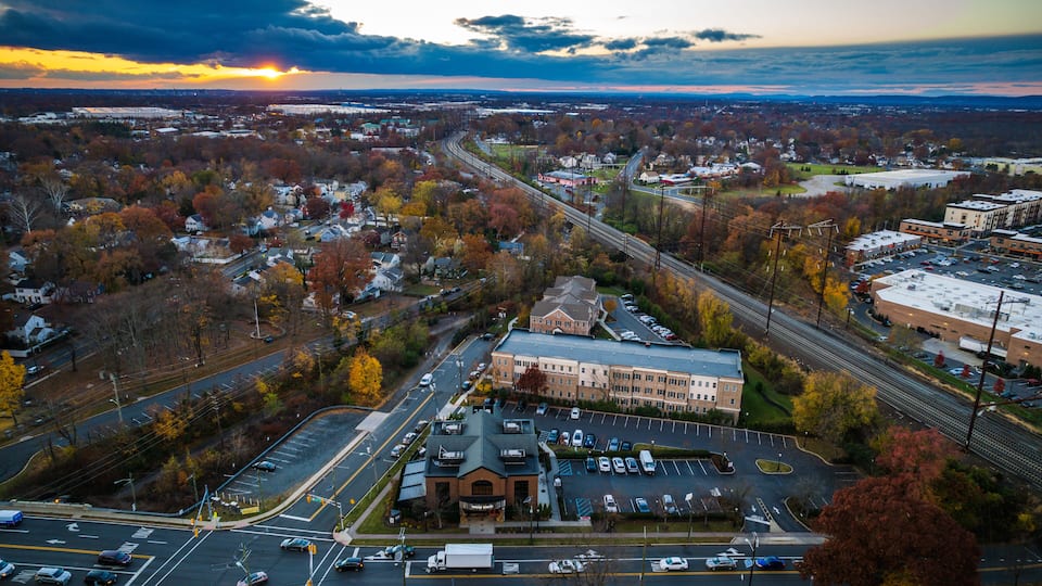 An aerial view of a town with a prominent building, a highway, and surrounding autumn foliage.