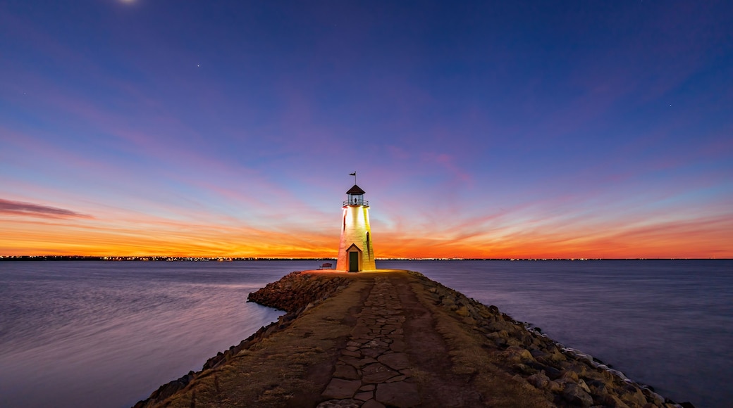 A lighthouse at dusk with a clear sky and calm water.