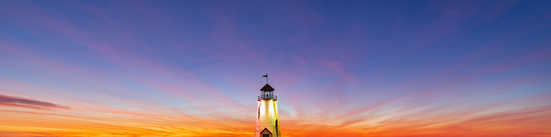 A lighthouse at dusk with a clear sky and calm water.
