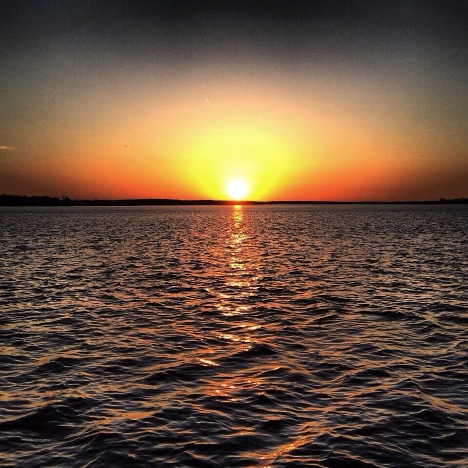 A sunset over a calm body of water with a visible horizon line.