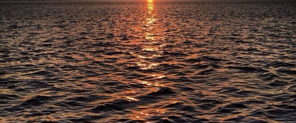 A sunset over a calm body of water with a visible horizon line.