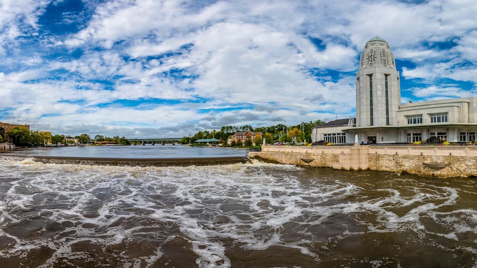 A river with waves, a bridge, and a large building with a tower.