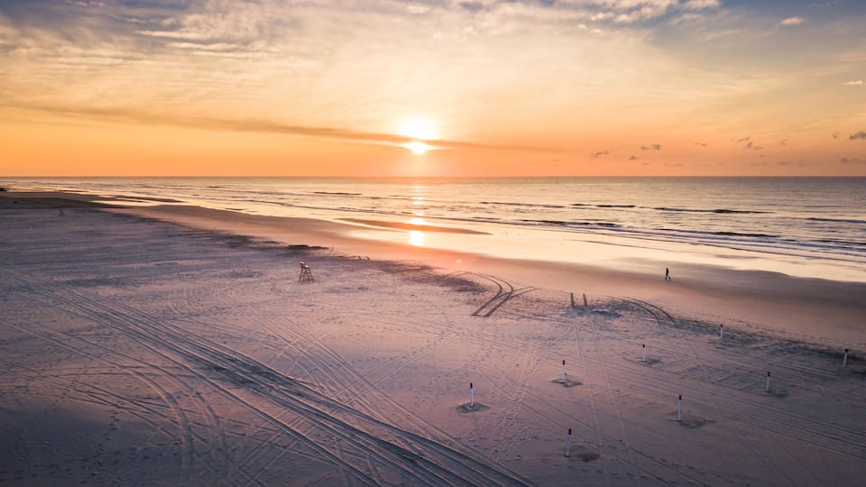 A beach at sunset with visible tire tracks and a few poles.